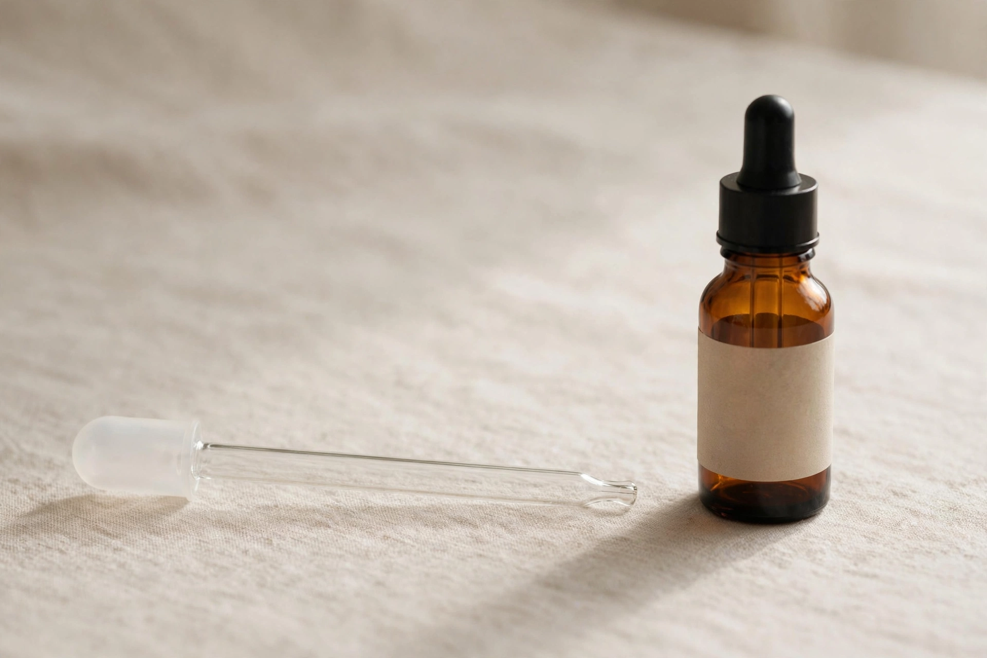 Glass dropper pipette beside a small amber CBD oil bottle on a beige surface