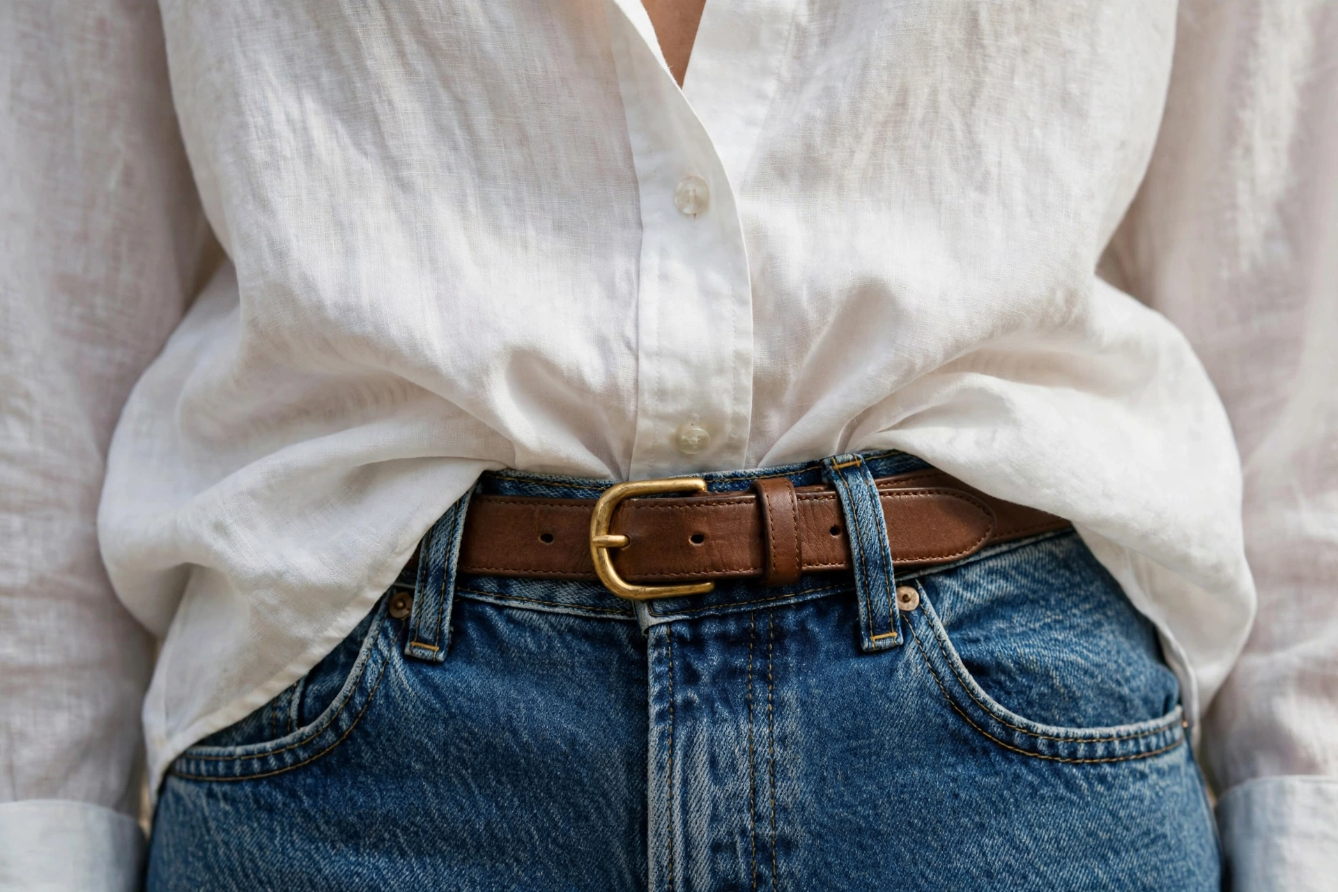 Front-tucked oversized white shirt styled with high-waisted jeans and a leather belt