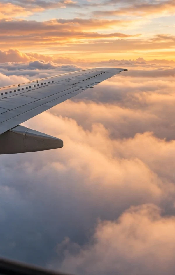 Airplane wing over clouds at golden sunrise inspiring budget travel hacks for cheap flights